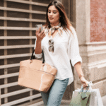 A woman walks down the street carrying shopping bags in both hands, smiling as she enjoys her day out.